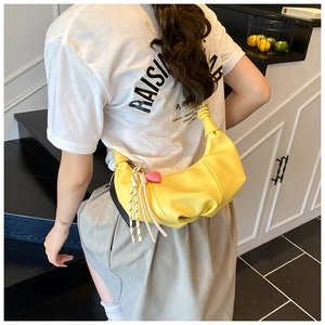 Detail of yellow crescent crossbody bag with heart charm and knotted strap shown on model