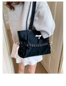 Detail view of black satin tote bag with pink bows and ruffled edges worn by model