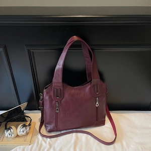 Detail of burgundy leather tote bag with silver zippers and laptop lifestyle backdrop