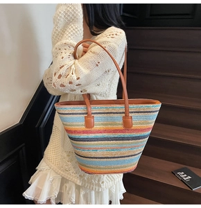 Detail der bunt gestreiften Stroh-Tote-Bag mit braunen Lederriemen auf Holztreppen