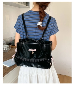 Detail of black satin tote bag featuring a pink bow, heart pendant, and ruffled bottom trim