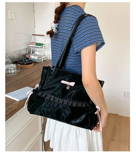 Detail of black glossy tote bag with pink bow and heart pendant on shoulder