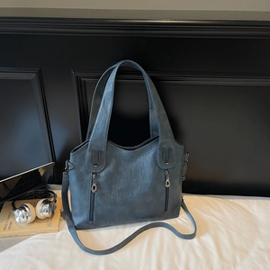 Detailed close-up of blue faux leather tote bag showing grainy texture and silver zippers