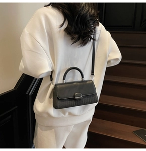 Detail of black crossbody bag showing textured leather finish and metal clasp on white hoodie