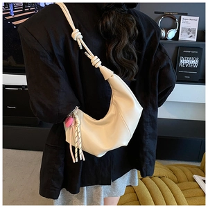 Detail of a creamy white crescent bag with knotted strap and pink heart pendant