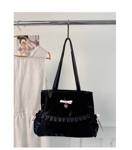 Detail of black glossy tote bag with pink bows and heart charm in balletcore style