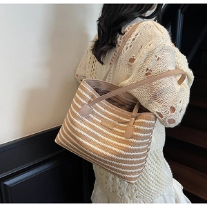 Détail d'un sac cabas en paille tressée avec rayures et des bandoulières en cuir robustes