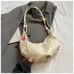 Detail of a beige crescent handbag with stylish knot strap and pink heart charm