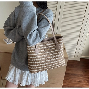 Détail d'un sac tressé arc-en-ciel avec poignées en cuir et plaque logo dorée