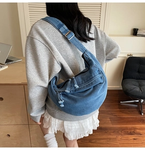 Detailed close-up of blue denim hobo bag with tassel zippers and metal hardware