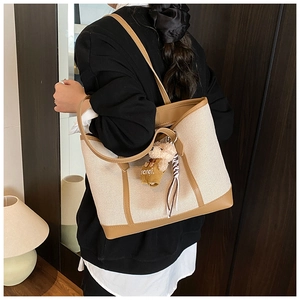 Detail of canvas tote bag with contrast leather trim, bear charm and ribbon accent