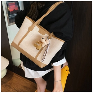 Detail of canvas tote bag showing brown leather trim and cute bear charm with ribbon