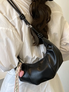 Minimalist black crescent crossbody bag with knotted shoulder strap and heart charm
