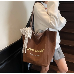 Detail of large brown canvas tote bag featuring cream printed text and lace bow charm
