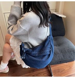 Detail of deep blue denim crescent crossbody bag shown with model in a home setting