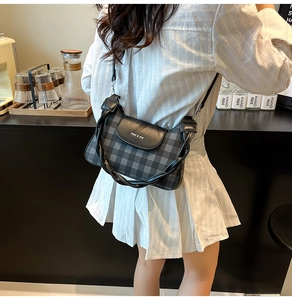Détail d'un sac à bandoulière à carreaux gris avec poignée torsadée et rabat magnétique