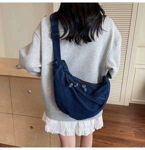 Detail of blue denim crescent crossbody bag with adjustable strap and tassel zipper on model