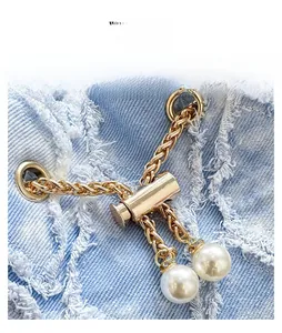 Detail of light gold drawstring lock with white faux pearls on blue denim fabric