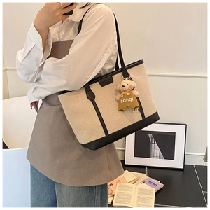 Detail of canvas tote bag with black leather trim and cute teddy bear charm accessory
