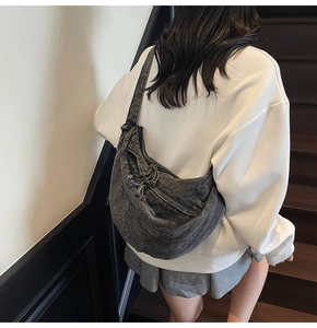 Detail of grey denim crossbody crescent bag with wash effect and knotted zipper pulls