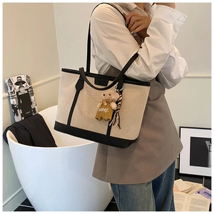 Detail of canvas tote bag with black leather trim, including a cute teddy bear charm