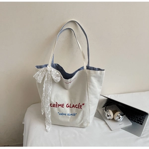 Detail of white canvas tote bag featuring lace ribbon bow and blue striped inner lining