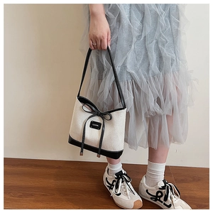 Detail view of woven cream tote bag with black leather trim and bow accent in a minimal room