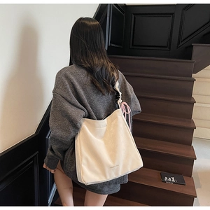 Detail of off-white tote bag with natural texture, pink tassel, and black strap