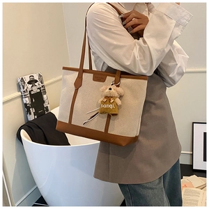 Detail of canvas tote bag with brown leather trim and cute teddy bear charm accessory