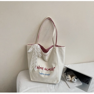 Detailed shot of white canvas tote with red stripe handles and lace bow on a desk