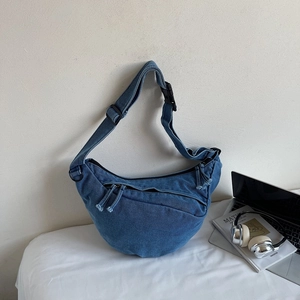 Detailed close-up of blue denim crescent crossbody bag with laptop and lifestyle props