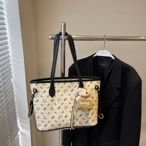 Détail du sac cabas blanc cassé avec motif ours et charm en peluche sur un blazer noir