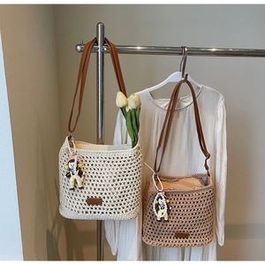 Detail of woven cutout tote bag in cream and tan colors with leather straps and doll charm