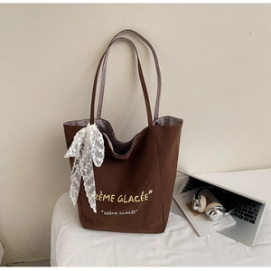 Detail of dark brown canvas tote bag with Crème Glacée text and lace bow accessory