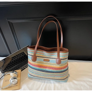 Détail d'un sac cabas en paille arc-en-ciel avec des anses marron sur un bureau