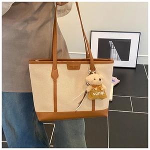 Detail of canvas tote bag with brown leather trim and cute plush bear charm accessory