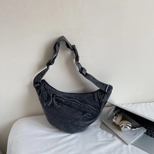 Detail of black washed denim crescent bag with multi-zipper pockets and long tassels