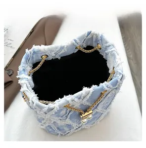 Detail view of denim bucket bag showing raw edge texture, pearl charms and gold chain strap