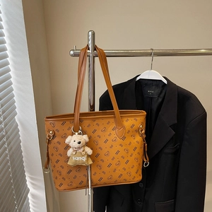 Détail d'un sac cabas marron avec imprimé ours et breloque peluche sur un costume noir