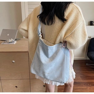 Detail view of a pale blue cloud-patterned tote bag worn by a model in a minimalist room