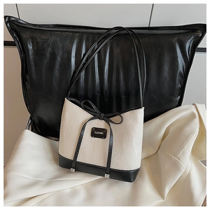 Close-up of contrast leather bow and metal logo tag on woven summer tote bag