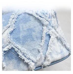 Detail view of light blue denim bucket bag with trendy raw edges and fringe stitching