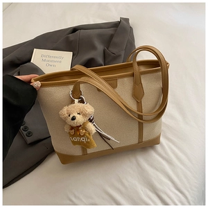 Detail view of canvas tote bag with brown leather trim and cute plush bear accessory