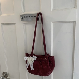 Détail d'un sac d'épaule en velours bordeaux avec un charme de perles en cœur et dentelle