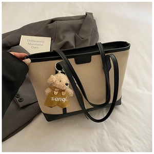 Detail of canvas tote bag with black leather trim and cute teddy bear charm on bed