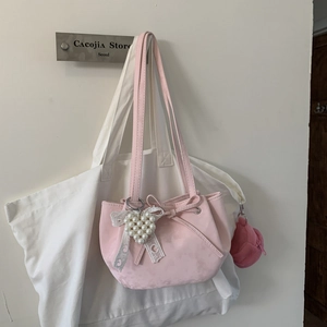 Détail du sac en daim rose avec nœud et breloque cœur en perles sur un sac en toile