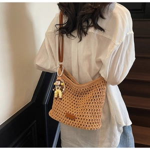 Detail of hollow woven straw tote bag with brown leather strap and cute doll pendant