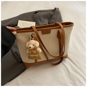 Detail of canvas tote bag with brown leather trim and cute teddy bear charm
