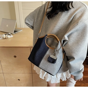 Detail of blue denim and gray fabric bucket bag with leather handles and mini charm