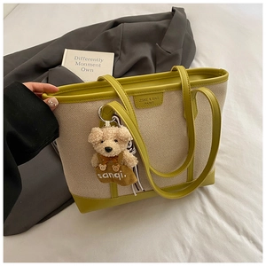 Detail of the large beige canvas and avocado green leather tote bag with a teddy bear charm